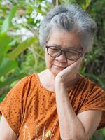 Sénior femme avec court blanc cheveux mal aux dents tandis que permanent dans une jardin. elle est mauvais pour la santé et a négatif pensées sur la vie fait du sa malheureux. concept de vieilli gens et voiture de santé photo