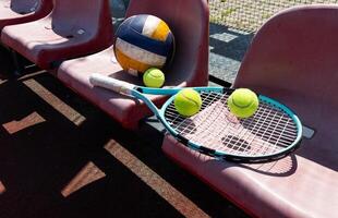 une tennis raquette, des balles et une volley-ball sur une banc sur le des sports tribune photo