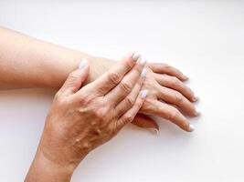 mains milieu âge femme avec blanc manucuré ongles doucement émouvant chaque autre sur blanc arrière-plan, Haut voir. plat allonger composition. soin de la peau et main se soucier ou mère l'amour concept. photo