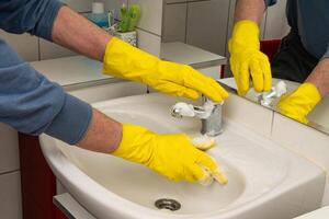 homme mains dans Jaune gants essuyage le évier dans le salle de bains. photo