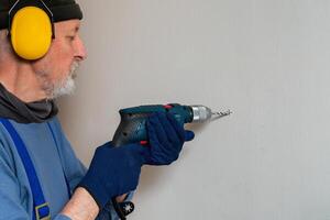 homme forage une trou dans le mur avec un électrique percer. photo