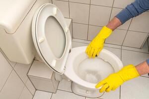 mains de une homme dans Jaune gants nettoyage le toilette bol dans le salle de bains photo