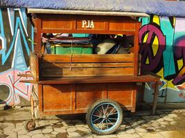 surakarta ville, central Java, Indonésie. avril 11, 2024. un vide fait maison en bois stalle Chariot sur le rue avec coloré graffiti art Contexte. Matin ambiance à début une vente activité. photo