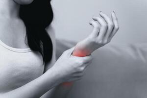 fermer de femme séance sur canapé détient sa poignet, main blessure avec rouge surligner photo