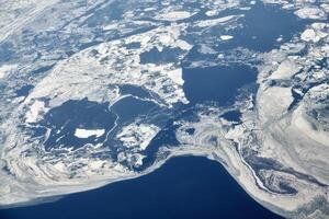 vue aérienne de la fenêtre de l'avion au-dessus des nuages jusqu'à la mer gelée couverte de neige, air frais d'hiver glacial photo