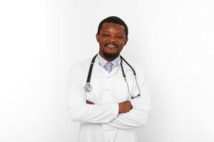 souriant noir barbu médecin homme franchi bras dans blanc peignoir avec stéthoscope, blanc Contexte photo