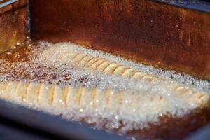 cuisson des pommes de terre frites en spirale dans de l'huile bouillante, riche en graisses et en calories fast food, délicieux malsain photo