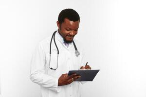 Homme médecin barbu noir en blouse blanche avec stéthoscope remplissant les dossiers médicaux sur le presse-papiers photo