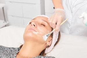 esthéticienne appliquant un masque de crème cosmétique sur le visage de la femme pour le rajeunissement, procédure dans un salon de beauté photo