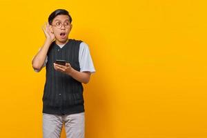 portrait d'un homme asiatique sérieux essayant d'entendre une conversation secrète et tenant un smartphone photo