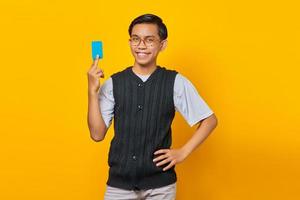 Portrait d'un homme asiatique séduisant riant et tenant une carte de crédit sur fond jaune photo
