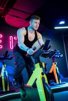 musclé actif homme dans tenue de sport formation cardio avec vélo. Beau fort homme cyclisme dans salle de sport. photo