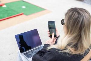 femme sur le golf cours avec téléphone intelligent avec des sports pari app photo