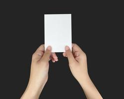 un gros plan de deux mains tenant un papier blanc vierge. montrant un modèle de carte de visite virtuelle sur fond noir. photo