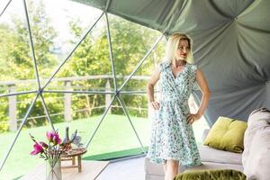 femme à la recherche en dehors à la nature de géo dôme tentes. vert, bleu, Orange Contexte. confortable, camping, glamping, vacances, vacances mode de vie concept. en plein air cabine avec scénique Contexte. photo