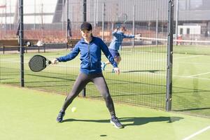 une fille dans tenue de sport est formation sur une pagayer tennis rechercher. le fille est frappe le Balle contre le verre à faire une rebond. concept de femmes en jouant pagayer. photo