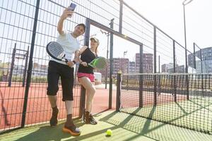 portrait de positif Jeune femme et adulte homme permanent sur padel tennis rechercher, en portant raquette et balle, souriant photo