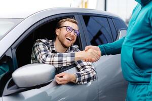 homme achat voiture et tremblement mains avec vendeur contre flou auto, fermer. concept de choisir et achat Nouveau voiture à salle d'exposition photo