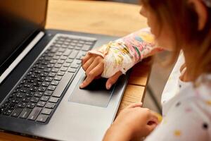 adolescent fille avec une cassé bras orthopédique jeter en train d'étudier en ligne photo