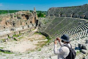 une Masculin touristique jouit une marcher par le amphithéâtre parmi le ruines de le ancien ville de Pergé, dans Turquie. le touristique regards autour le ancien ville de pergé avec fascination et prend photographies photo