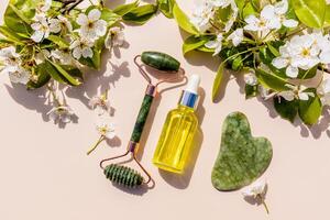 rouleau masseur, gua sha grattoir fabriqué de Naturel calcul, pétrole dans une bouteille avec une pipette parmi le floraison branches de le fruit arbre. Naturel se soucier. photo