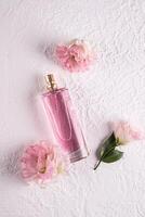 une élégant grand bouteille de aux femmes parfum sur une blanc Contexte avec fleurs . verticale voir. présentation de le délicat fragrance de parfum. photo
