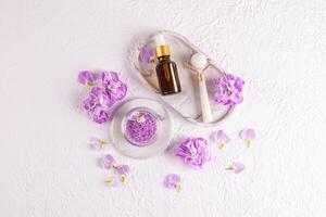 une ensemble de cosmétique pétrole ou sérum pour massage, une rouleau fabriqué de blanc pierre sur une plateau. Haut voir. lilas délicat fleurs et une baignoire sels. spa traitements. photo