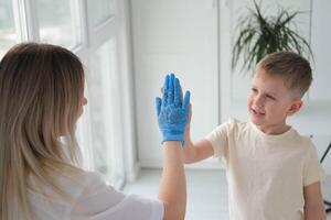 le médecin donne cinq mains à le garçon. le pédiatre trouve contact avec le enfant pendant le examen. photo