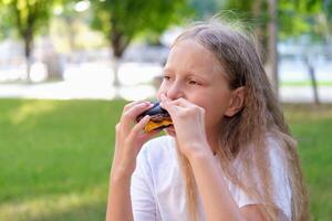 le enfant mange une noir Burger sur le rue. le fille mord de pièces de une cheeseburger. vite nourriture photo