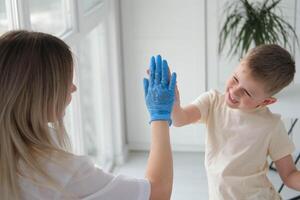 le médecin donne cinq mains à le garçon. le pédiatre trouve contact avec le enfant pendant le examen. photo