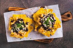 proche en haut de mexicain cuit Nachos avec poulet, noir des haricots et fromage sur une planche Haut vue photo