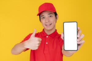 souriant livraison homme montrant téléphone intelligent écran et faire des gestes pouce en haut photo