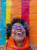 une femme dans électrique bleu lunettes des rires joyeusement par une coloré brique mur photo