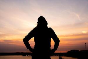 silhouette de un méconnaissable fille à le coucher du soleil dans une port photo