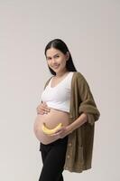 portrait de magnifique Enceinte femme en portant banane plus de blanc Contexte studio, santé et maternité concept photo