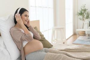 content Enceinte femme avec écouteurs écoute à Mozart la musique et mensonge sur lit, grossesse concept photo