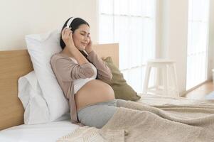 content Enceinte femme avec écouteurs écoute à Mozart la musique et mensonge sur lit, grossesse concept photo