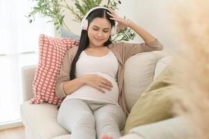 content Enceinte femme avec écouteurs écoute à Mozart la musique et mensonge sur canapé, grossesse concept photo