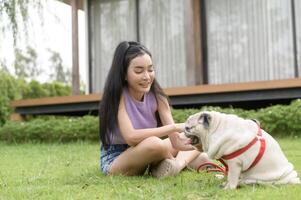 content asiatique femme en jouant avec mignonne intelligent carlin chiot chien dans le arrière-cour photo