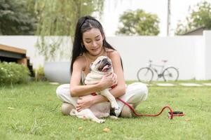 content asiatique femme en jouant avec mignonne intelligent carlin chiot chien dans le arrière-cour photo