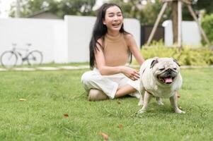 content asiatique femme en jouant avec mignonne intelligent carlin chiot chien dans le arrière-cour photo