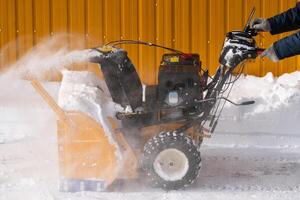 homme en utilisant souffleuse à neige à retirer neige après hiver tempête. il est assisté par une neige lanceur sur une hiver route photo