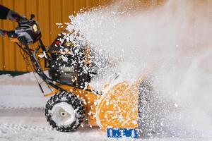 une Masculin ouvrier est en utilisant une souffleuse à neige machine à clair neige de le route après une hiver orage photo