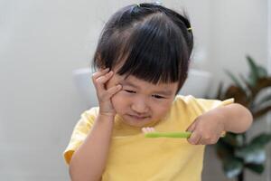 peu asiatique fille presses main à joue, souffre de douleur dans dent. les dents carie, dentaire problèmes, enfant émotions et faciale expression, oral santé se soucier, réduire bonbons, fluor enrobage photo