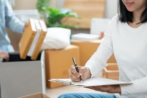 bouge toi loger, déménagement. femme en utilisant Ménage liste de contrôle pour Nouveau appartement à l'intérieur le pièce sont papier carton des boites contenant personnel affaires et meubles. bouge toi dans une maison ou condominium photo