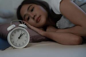 asiatique femme dans lit en retard en essayant à sommeil Souffrance insomnie, sans sommeil ou effrayé dans une cauchemar, à la recherche triste inquiet et stressé. fatigué et mal de crâne ou migraine veille en haut dans le milieu de le nuit. photo