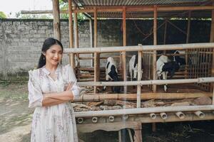 souriant Jeune asiatique femme permanent dans de face de traditionnel cage fabriqué de bois et bambou dans Indonésie rural zone avec chèvre à l'intérieur photo