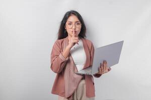 Jeune asiatique affaires femme en mettant une doigt dans de face de lèvres faire des gestes rester silencieux ou rester silencieux tandis que en portant ordinateur portable, isolé par blanc Contexte. photo