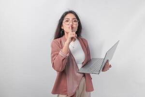 Jeune asiatique affaires femme en mettant une doigt dans de face de lèvres faire des gestes rester silencieux ou rester silencieux tandis que en portant ordinateur portable, isolé par blanc Contexte. photo