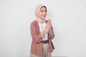 élégant asiatique musulman femme portant voile hijab souriant à le caméra et faire des gestes traditionnel salutation isolé plus de blanc Contexte. photo